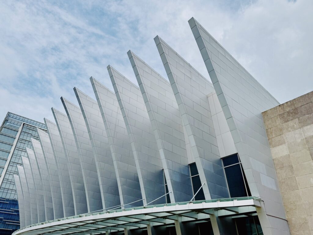 Row of angled white roof fins on a modern convention center rising against a cloudy blue sky