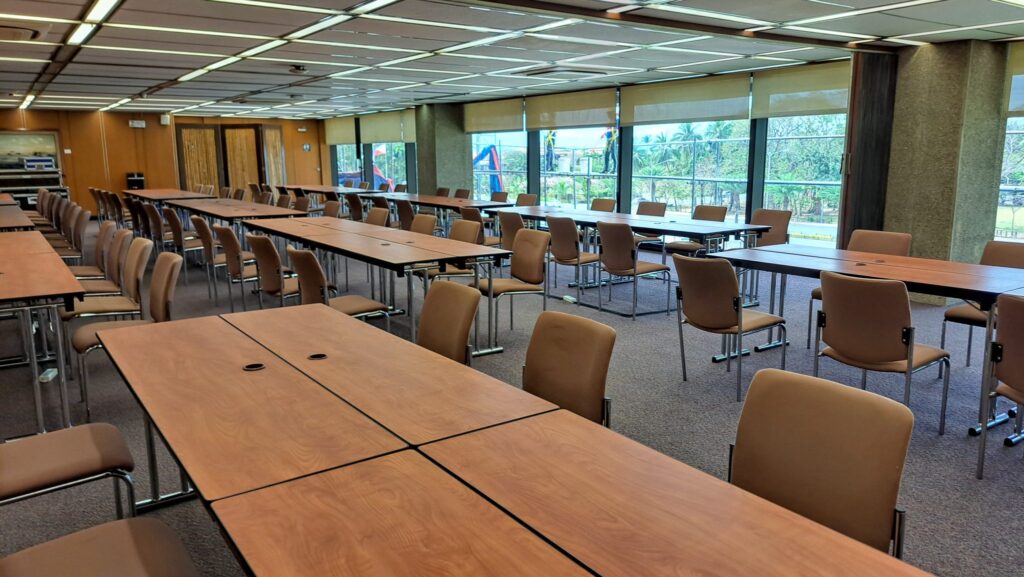 Long wooden tables and brown chairs in an empty meeting room with a wall of windows