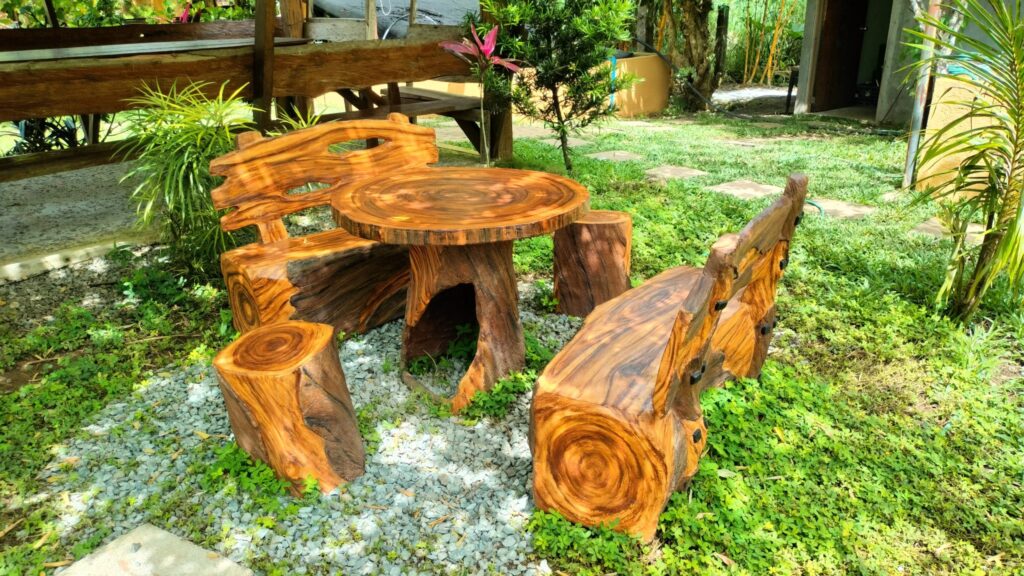 Carved wooden table and benches made from tree trunks standing on a green lawn in a garden