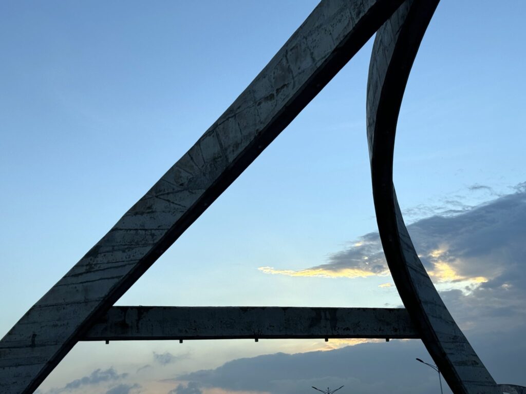 Curved concrete beams of a modern structure framing a blue evening sky with soft clouds